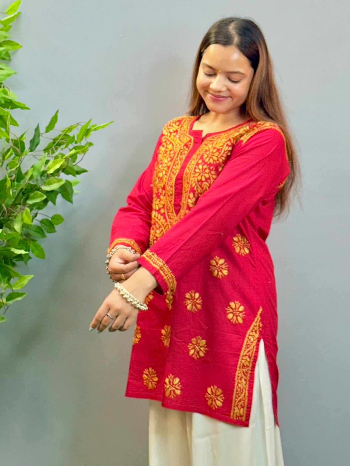 Model wearing a rust red cotton short kurta with golden Lucknowi chikankari embroidery, paired with white palazzo pants.