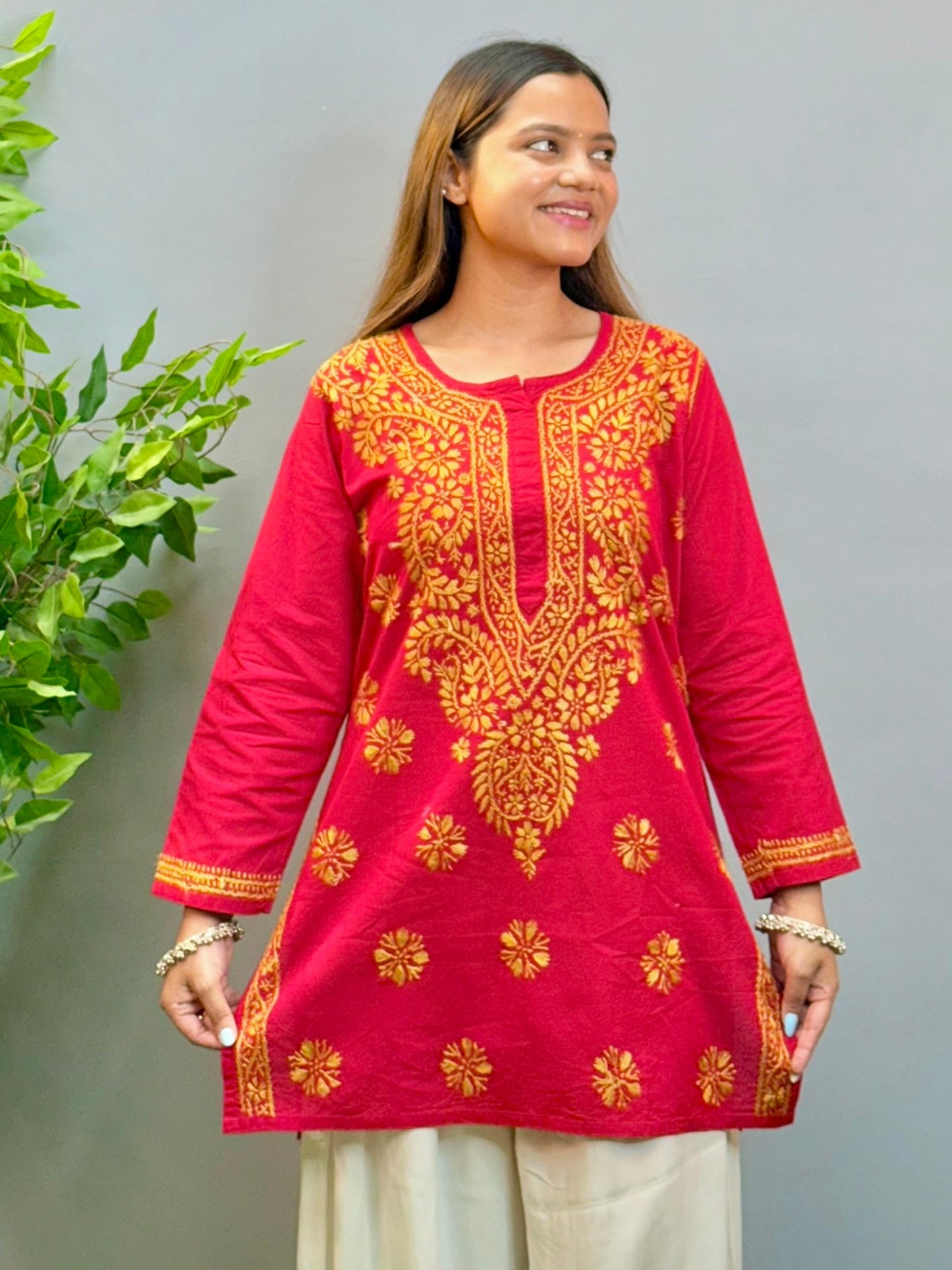 Model wearing a rust red cotton short kurta with golden Lucknowi chikankari embroidery, paired with white palazzo pants.