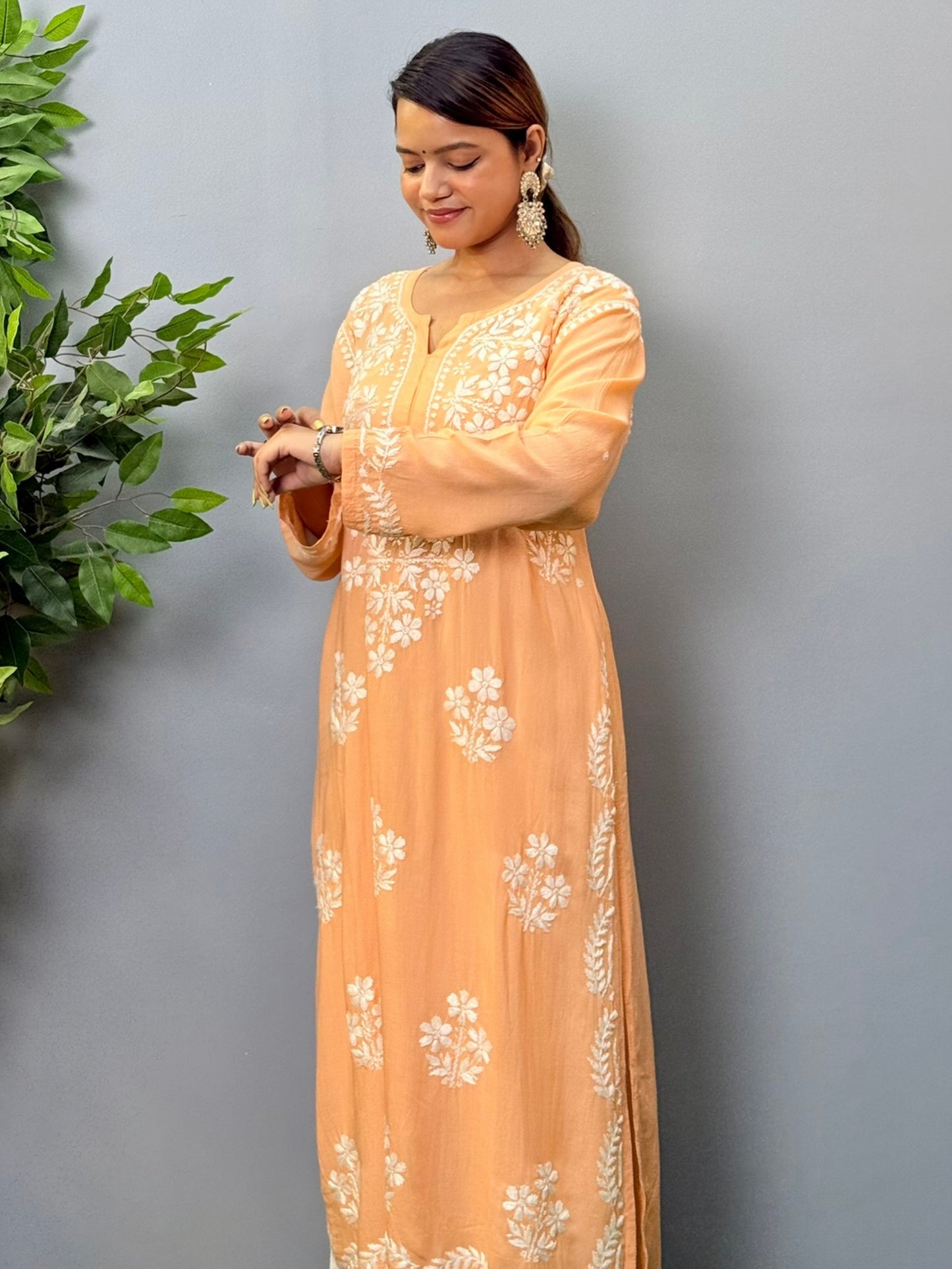 Model wearing a peach orange modal chikankari kurta with detailed white floral hand embroidery