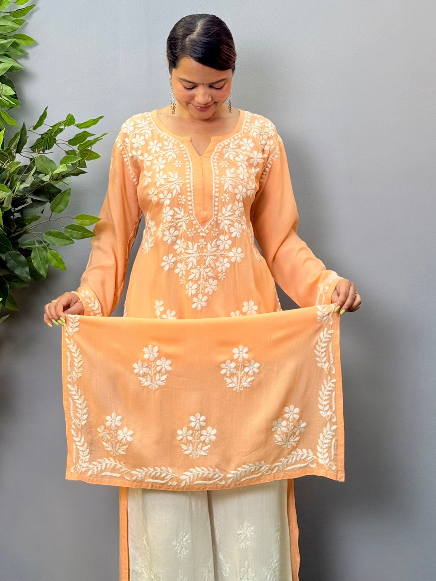 Model wearing a peach orange modal chikankari kurta with detailed white floral hand embroidery