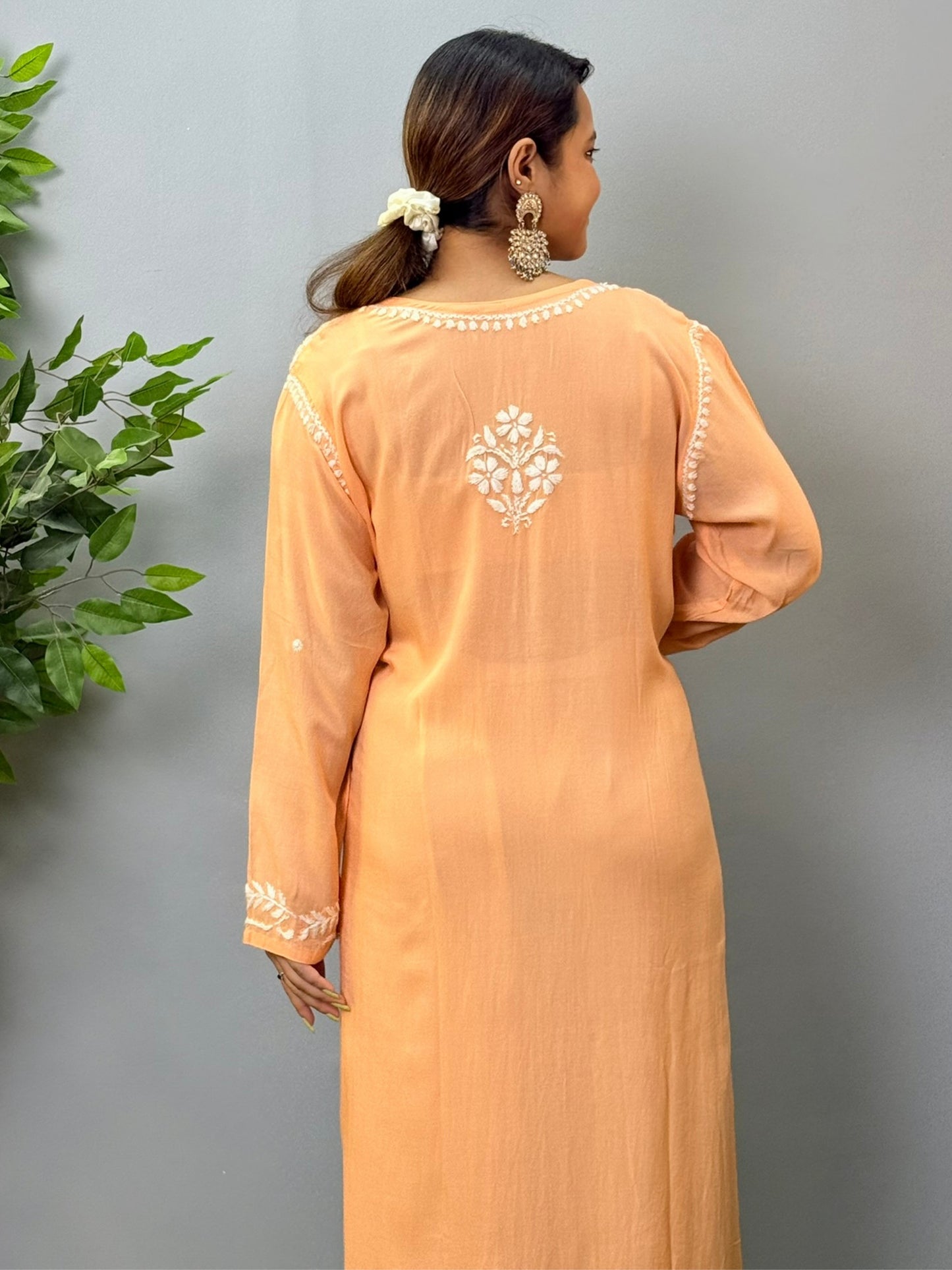 Model wearing a peach orange modal chikankari kurta with detailed white floral hand embroidery