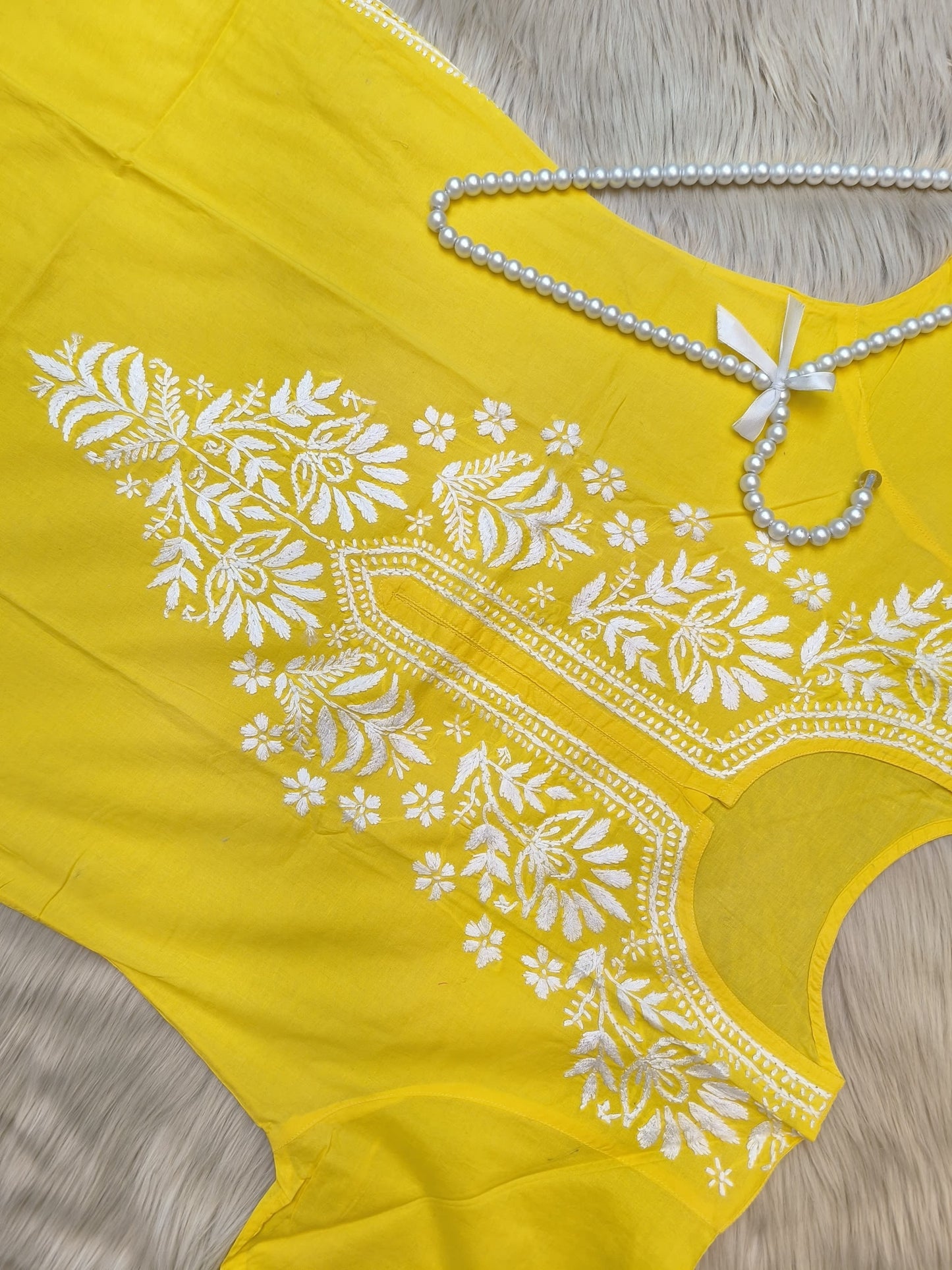 Sunshine yellow cotton chikankari kurta with white hand embroidery laid flat on beige fur background