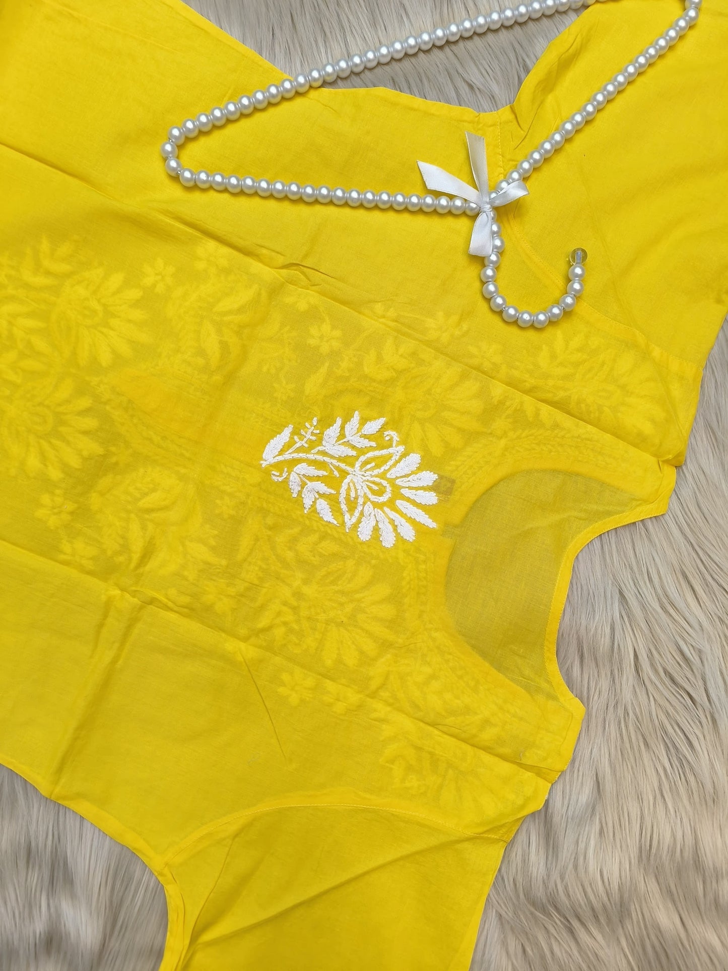 Sunshine yellow cotton chikankari kurta with white hand embroidery laid flat on beige fur background
