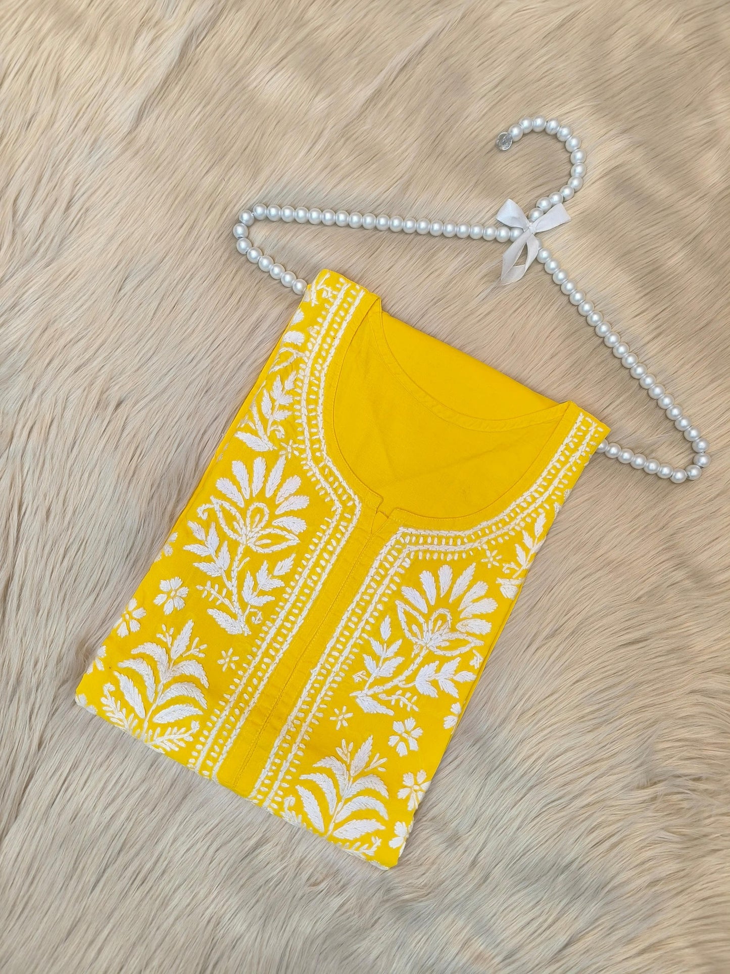 Sunshine yellow cotton chikankari kurta with white hand embroidery laid flat on beige fur background
