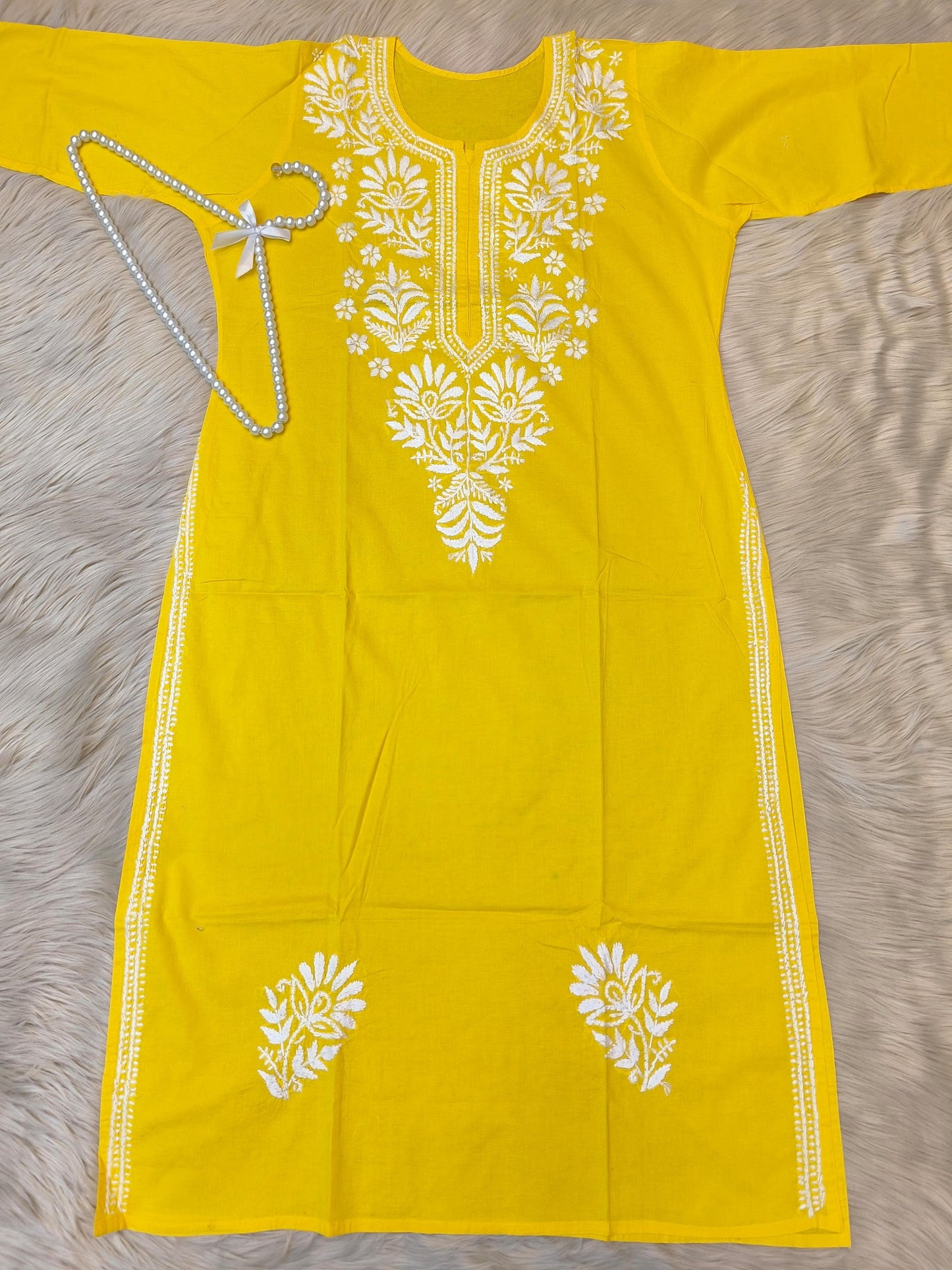 Sunshine yellow cotton chikankari kurta with white hand embroidery laid flat on beige fur background