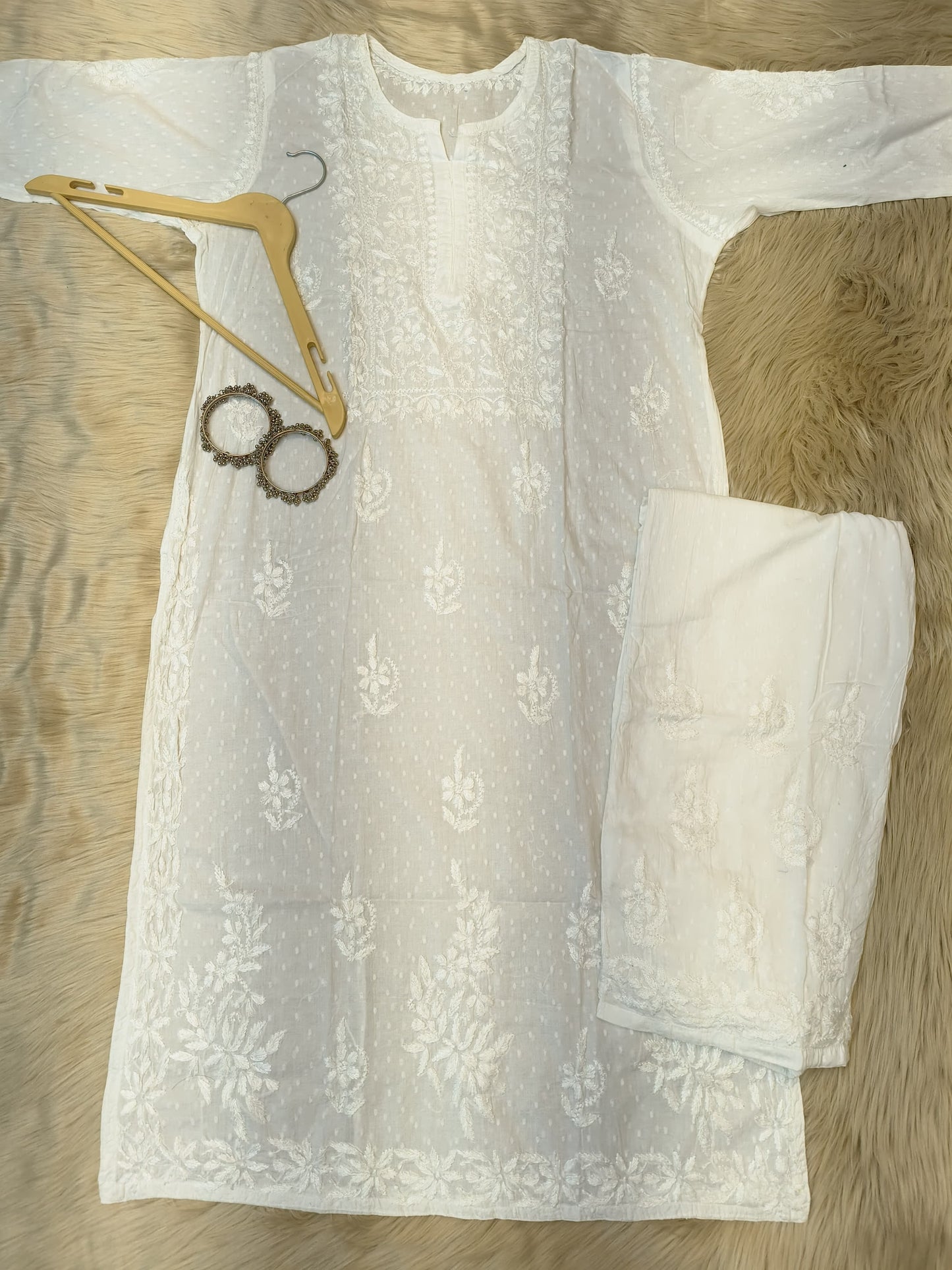 White Chikankari dobby cotton kurta with matching palazzo, bangles and hanger placed on fur background