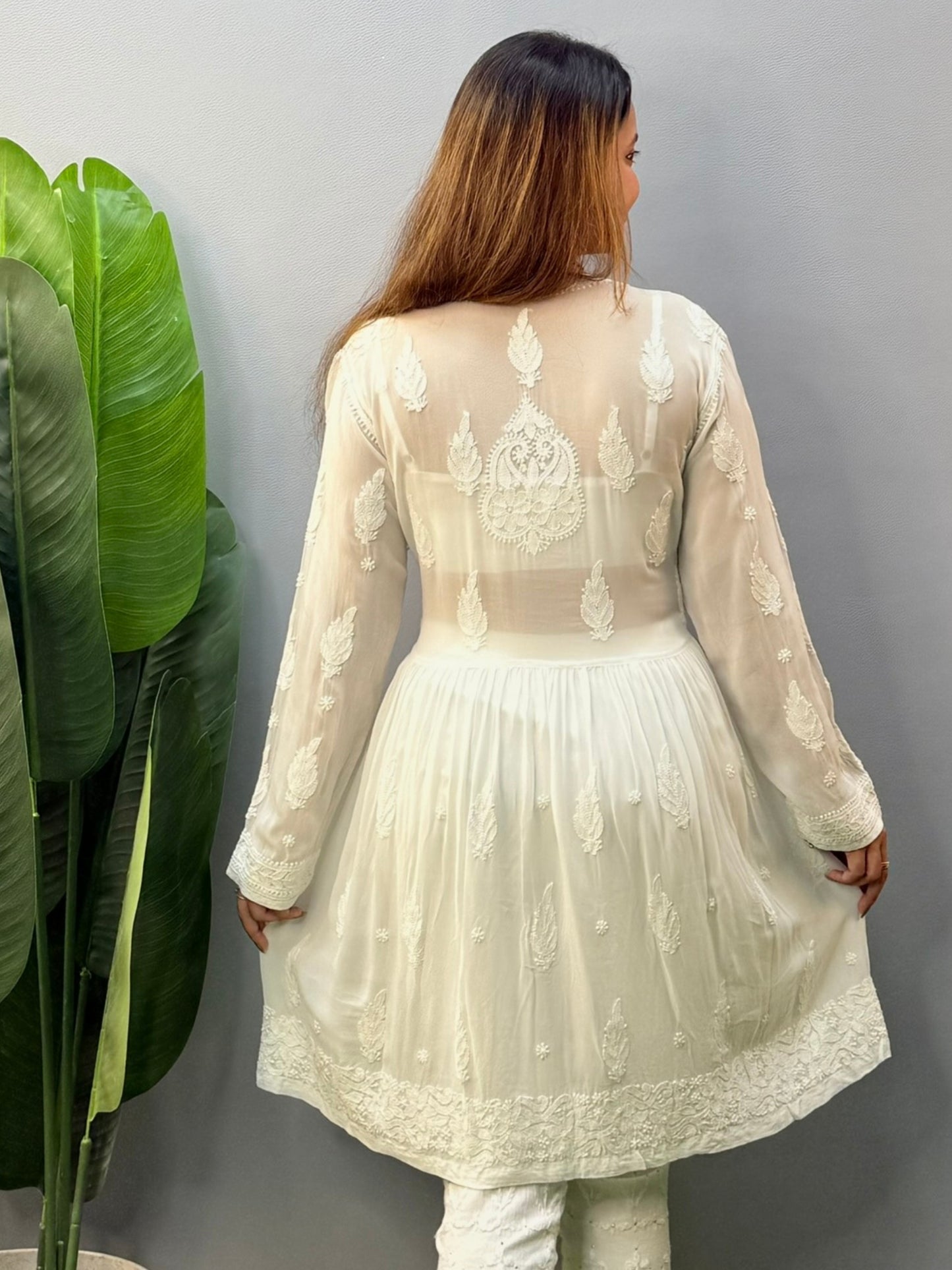 Model wearing a white flared chikankari short kurta with all-over hand embroidery in viscose fabric