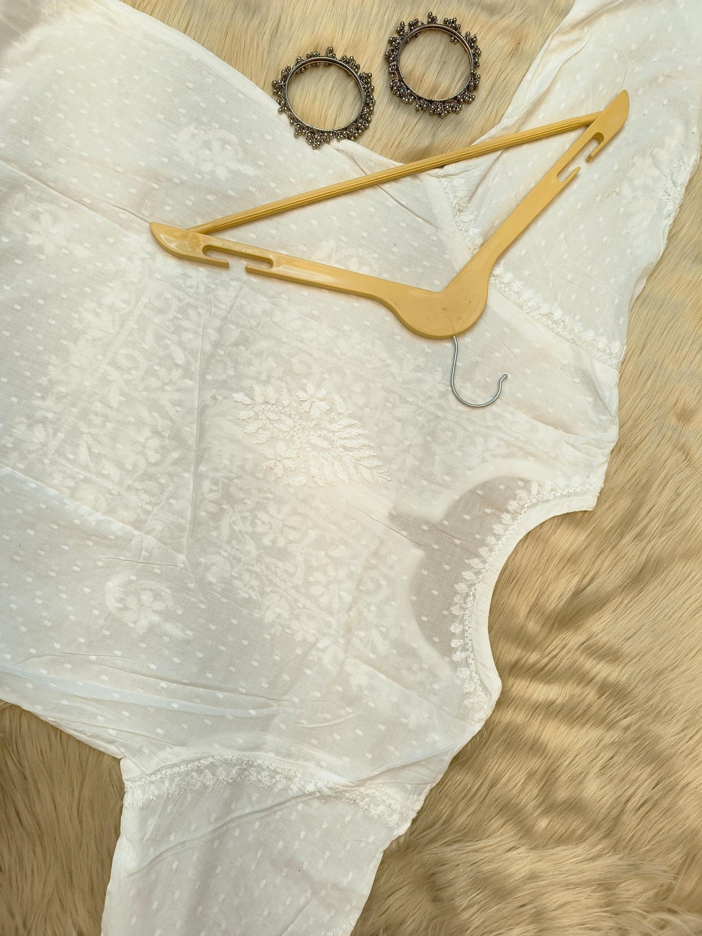 White Chikankari dobby cotton kurta with matching palazzo, bangles and hanger placed on fur background