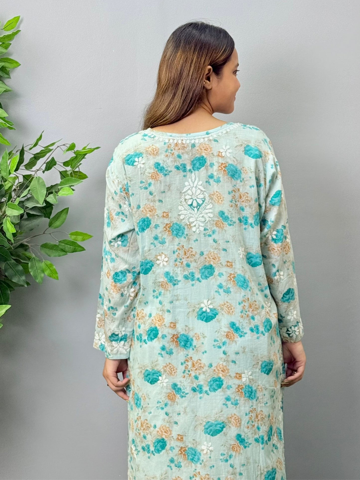 Aqua blue floral printed mulmul chikankari kurta with white embroidery worn by a woman standing on green grass
