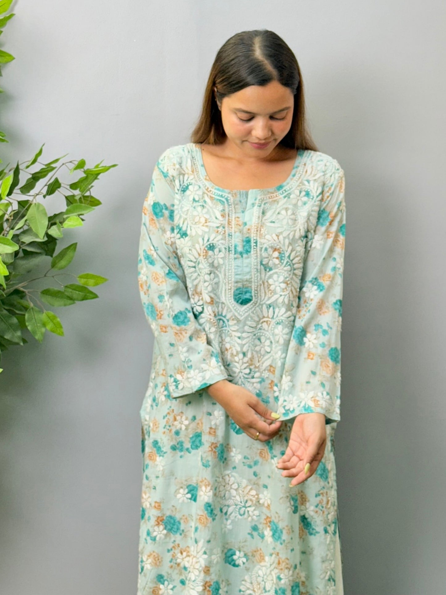 Aqua blue floral printed mulmul chikankari kurta with white embroidery worn by a woman standing on green grass