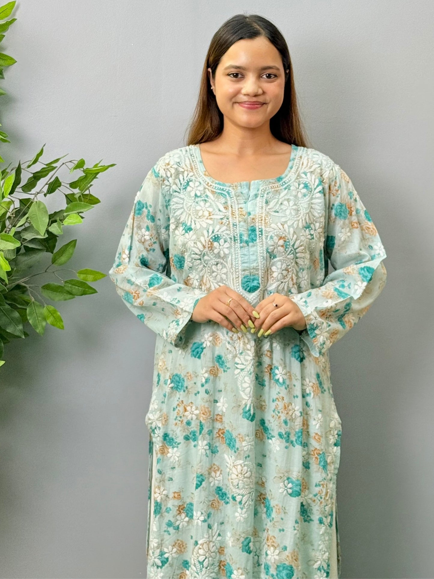 Aqua blue floral printed mulmul chikankari kurta with white embroidery worn by a woman standing on green grass