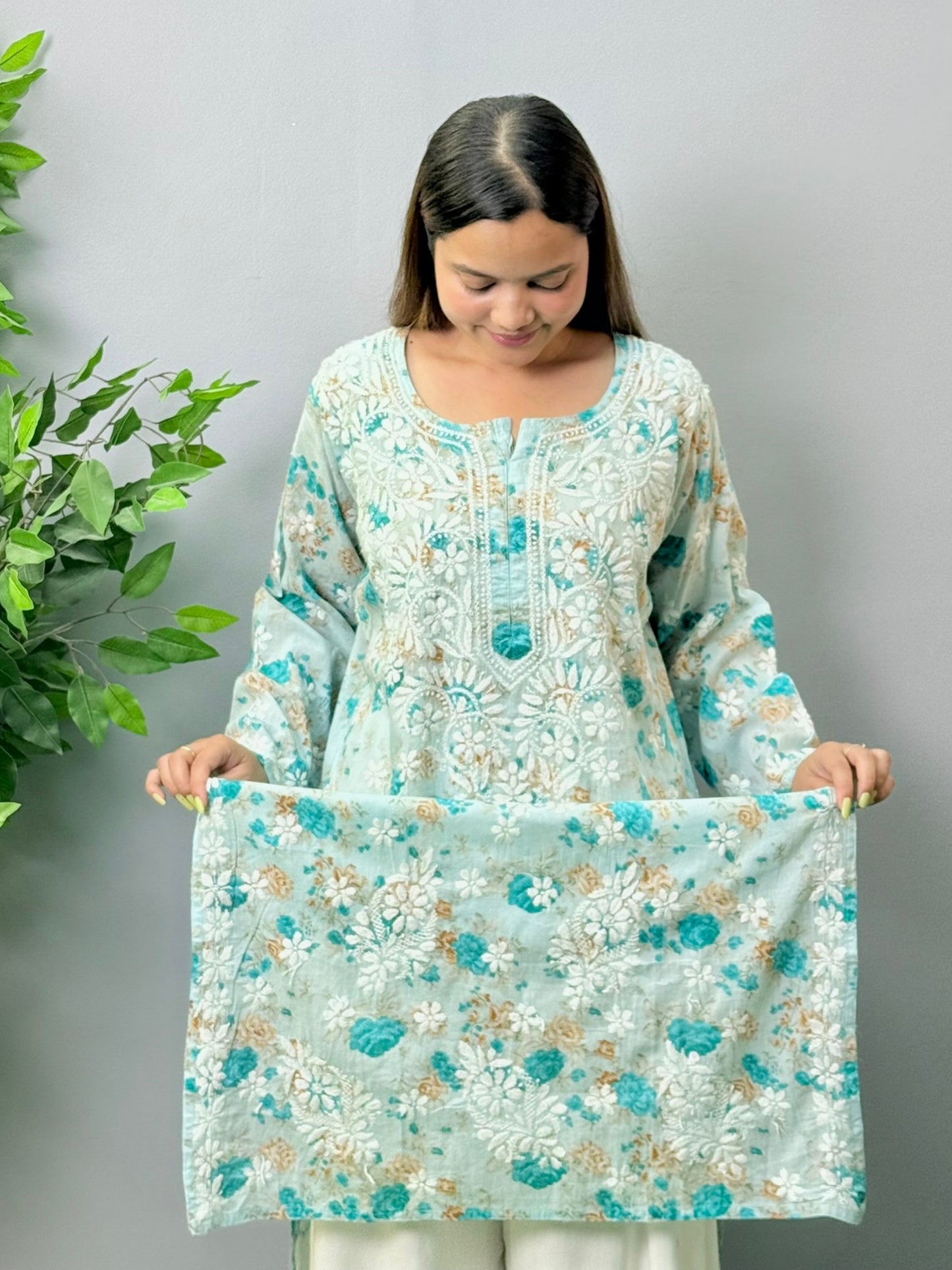 Aqua blue floral printed mulmul chikankari kurta with white embroidery worn by a woman standing on green grass