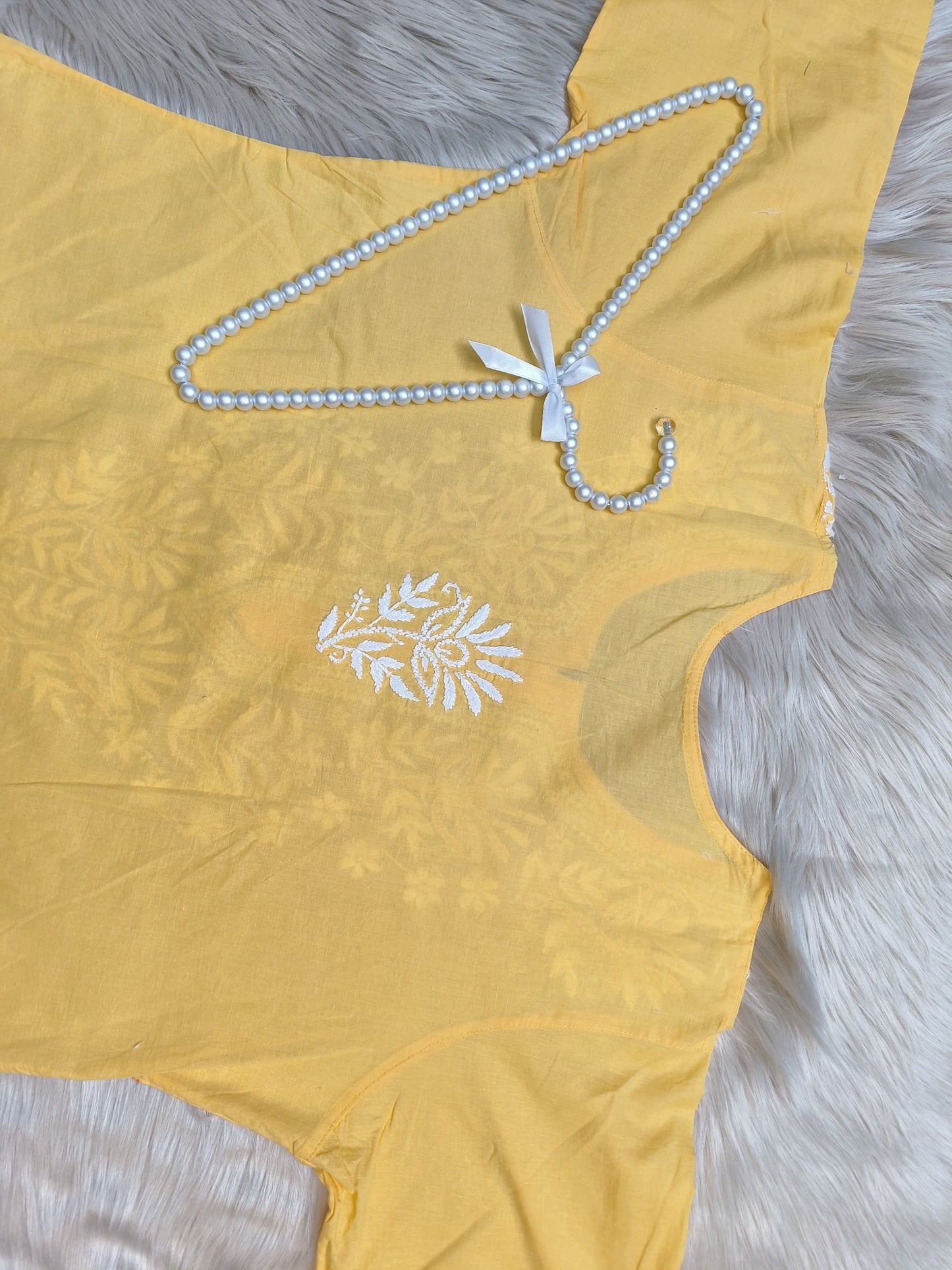 Yellow cotton kurta with white Lucknowi Chikankari hand embroidery displayed flat on fur background with pearl hanger