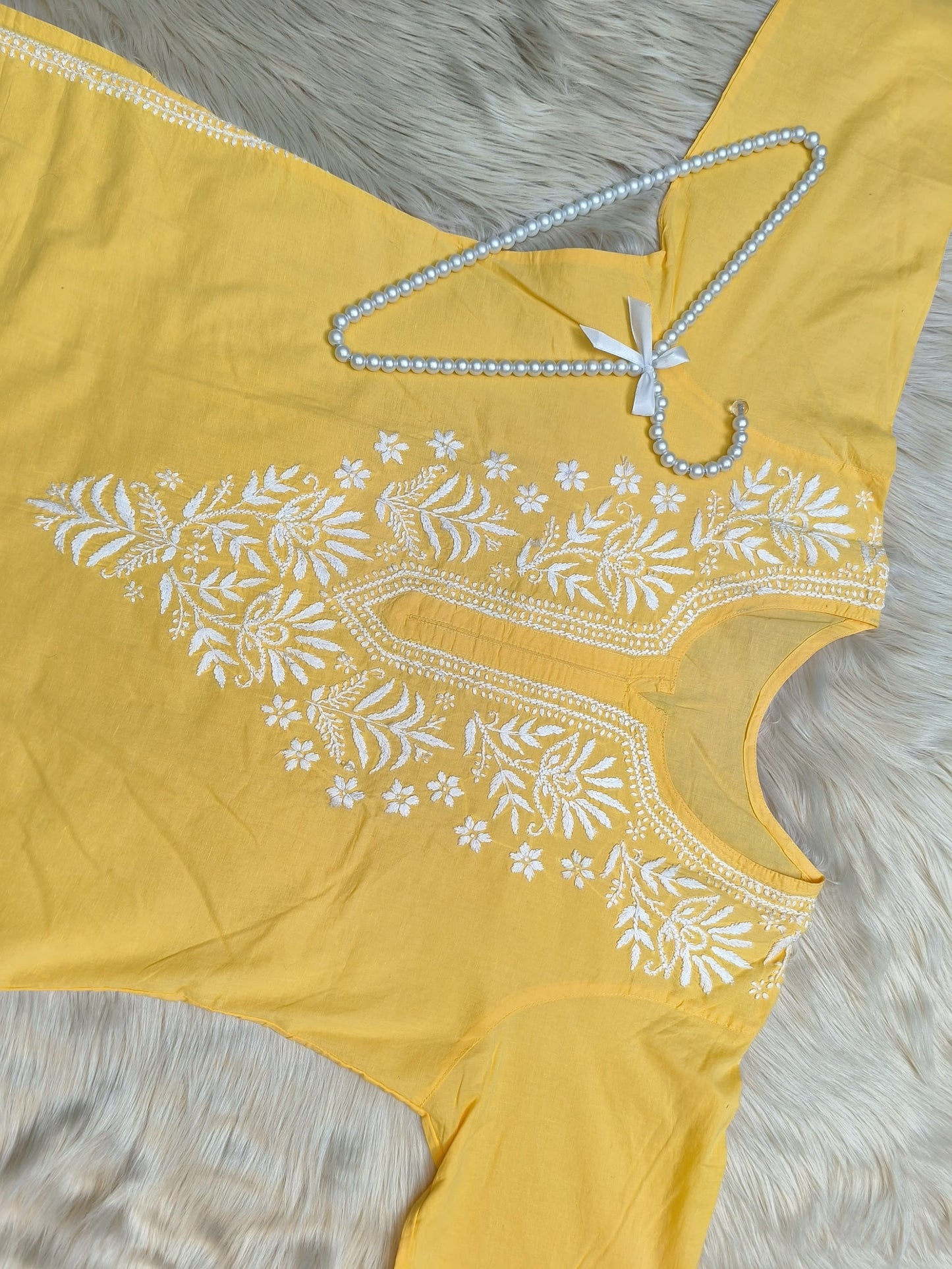 Yellow cotton kurta with white Lucknowi Chikankari hand embroidery displayed flat on fur background with pearl hanger