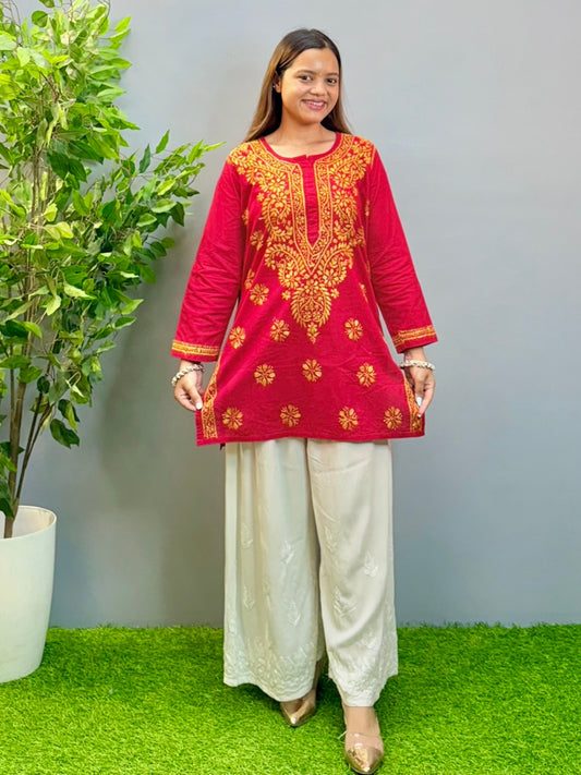 Model wearing a rust red cotton short kurta with golden Lucknowi chikankari embroidery, paired with white palazzo pants.