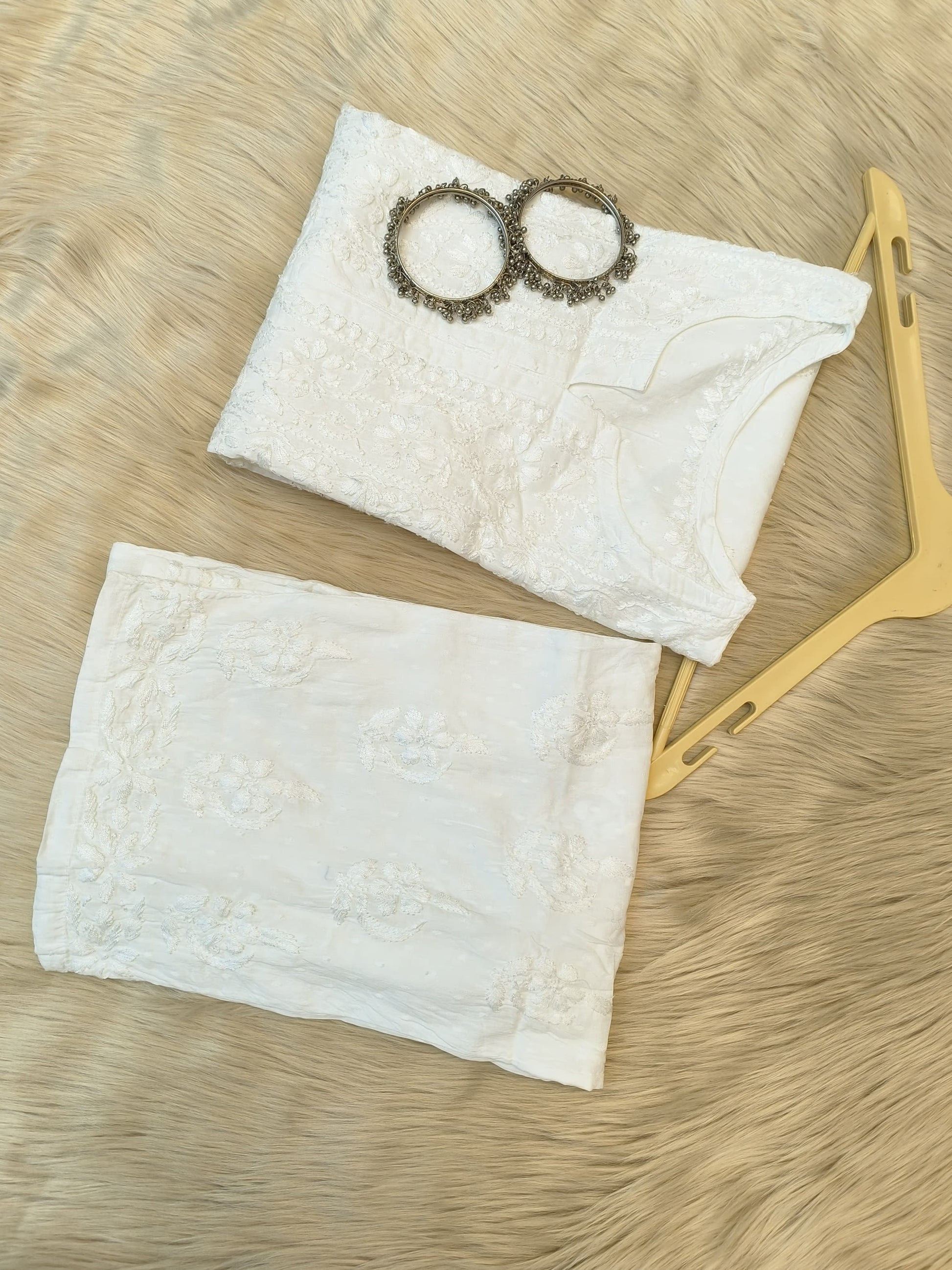 White Chikankari dobby cotton kurta with matching palazzo, bangles and hanger placed on fur background