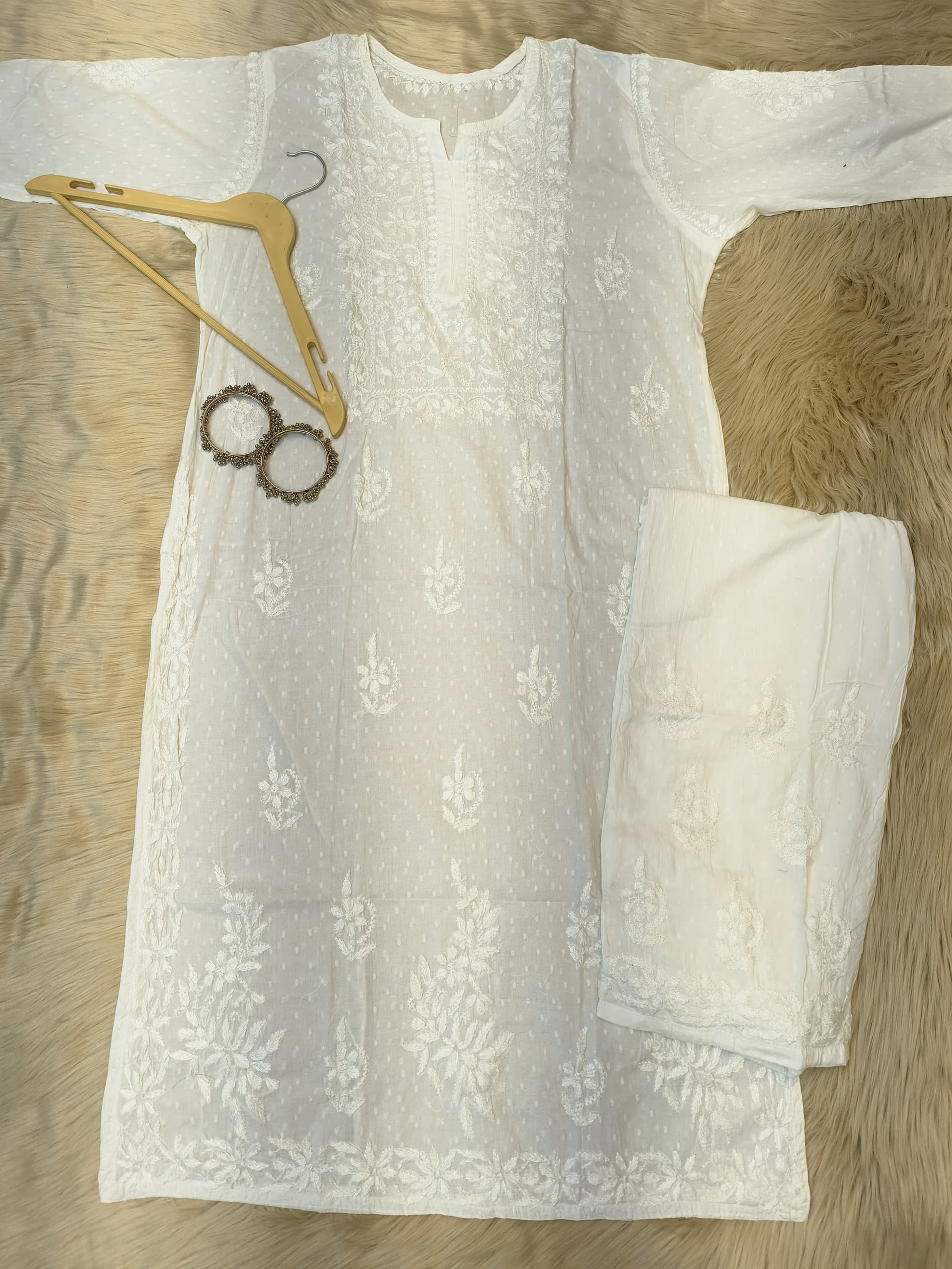 White Chikankari dobby cotton kurta with matching palazzo, bangles and hanger placed on fur background