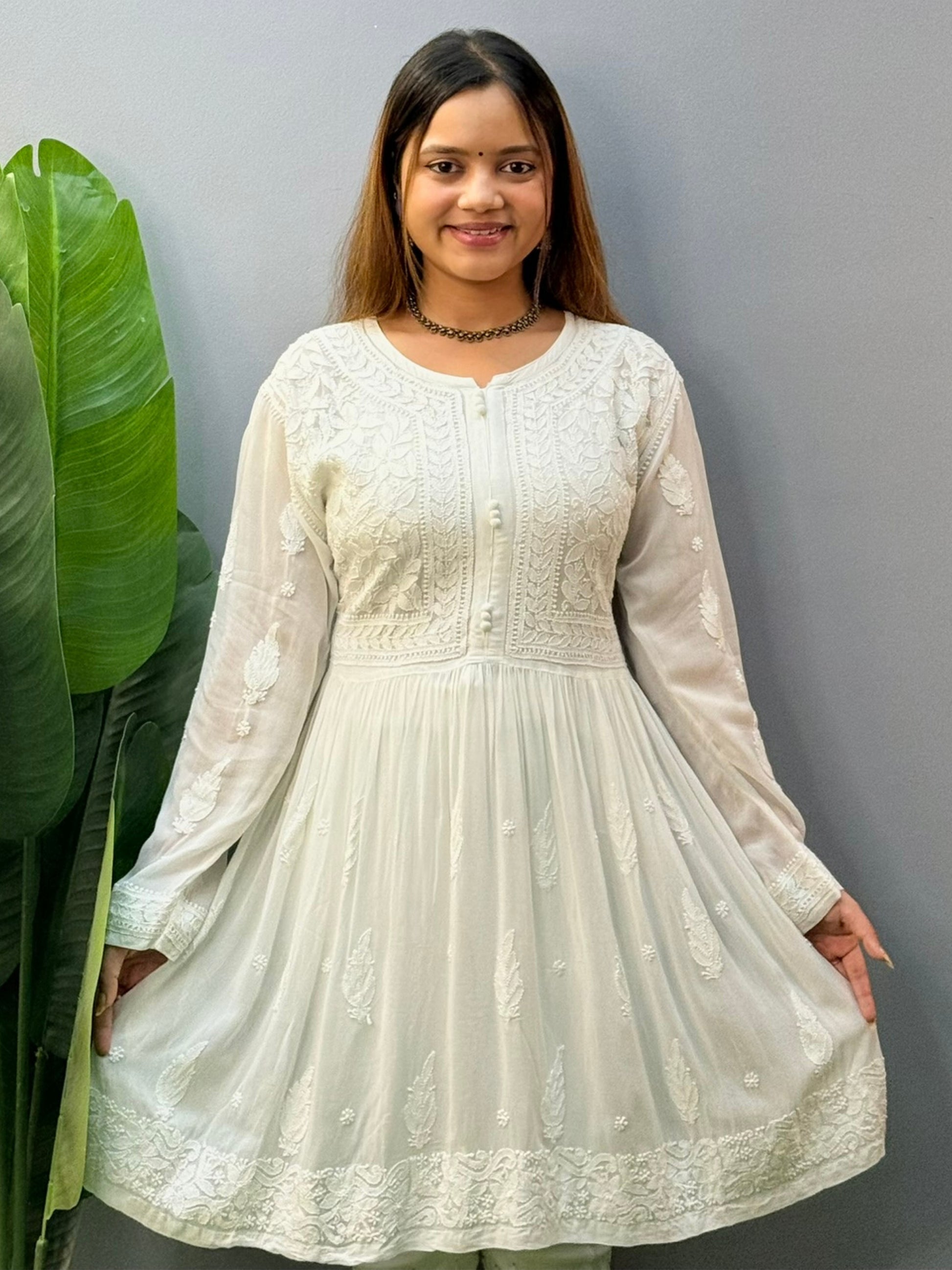 Model wearing a white flared chikankari short kurta with all-over hand embroidery in viscose fabric