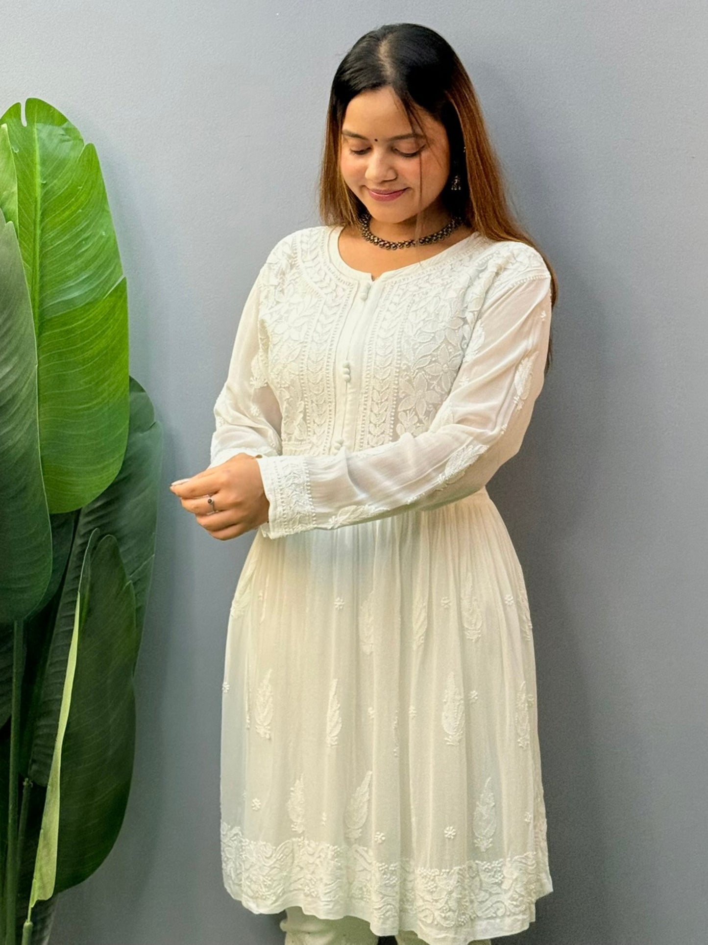 Model wearing a white flared chikankari short kurta with all-over hand embroidery in viscose fabric